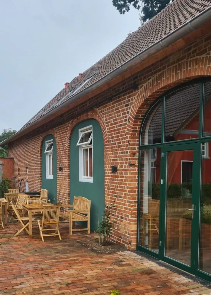 Klinkerscheune nach der Sanierung mit grün gerahmter Rundbogenverglasung und Terrasse
