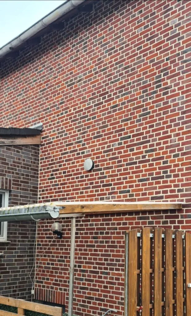 Sanierte Klinkerhauswand mit gleichmäßigem Fugenbild oberhalb eines schmalen Vordachs