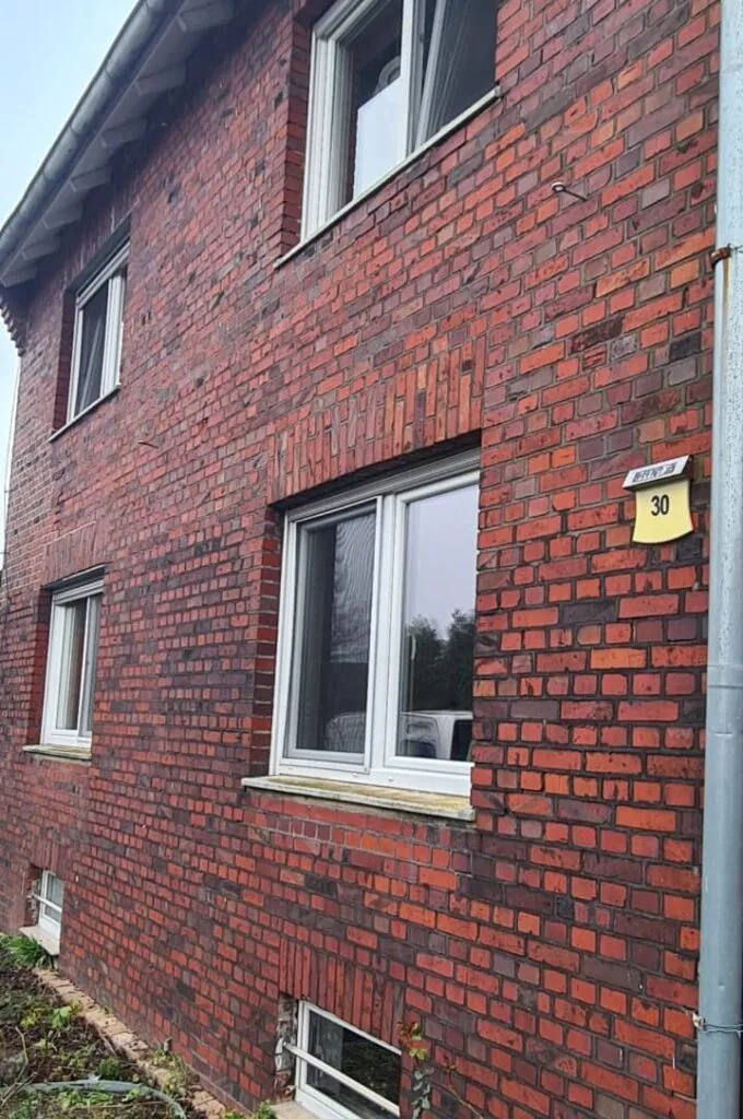 Rote Klinkerfassade mit dunklen Fugen und weißen Fenstern vor der Sanierung