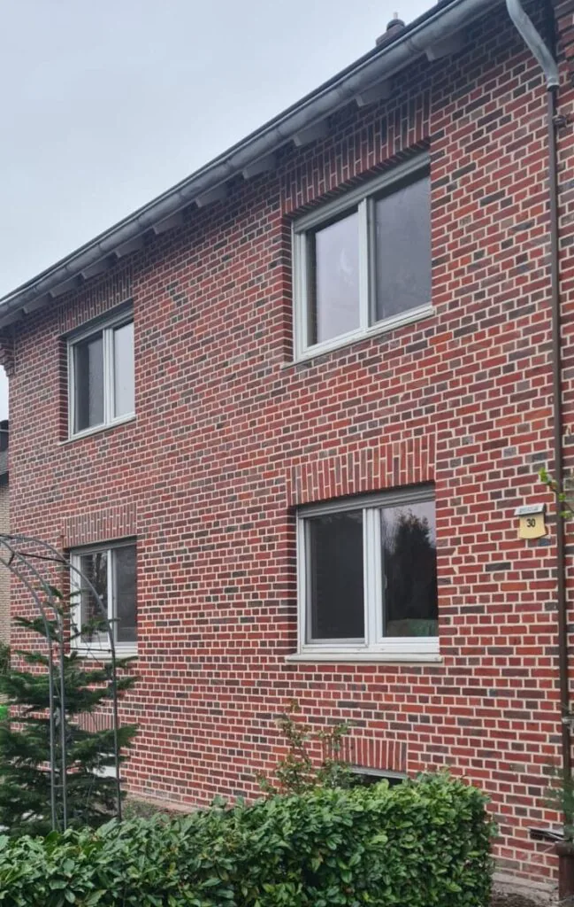 Sanierte rote Klinkerfassade mit hellen Fugen und weißen Fensterrahmen