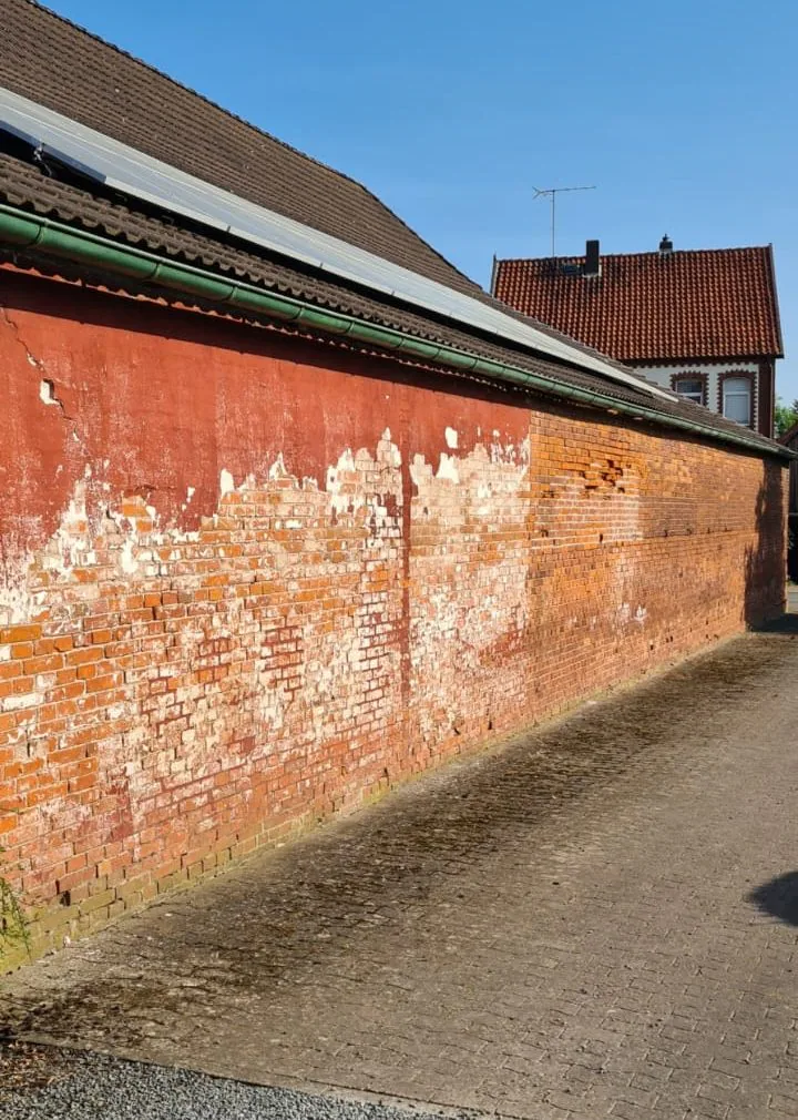 Lange rote Klinkerwand mit großflächigen hellen Rückständen vor der Sanierung