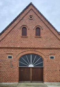 Giebel einer Klinkerscheune mit Fächerfenster und Holztor nach der Sanierung