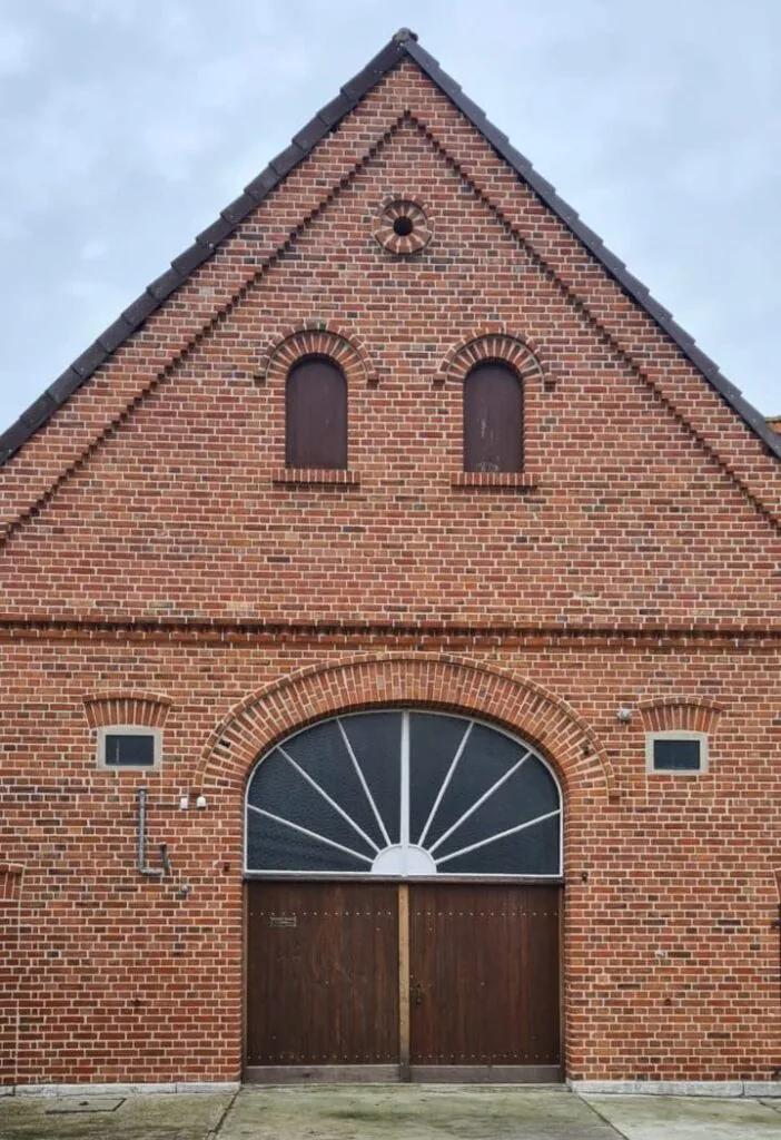 Sanierter Klinkergiebel mit zwei Bogenfenstern und Fächerfenster über dem Holztor
