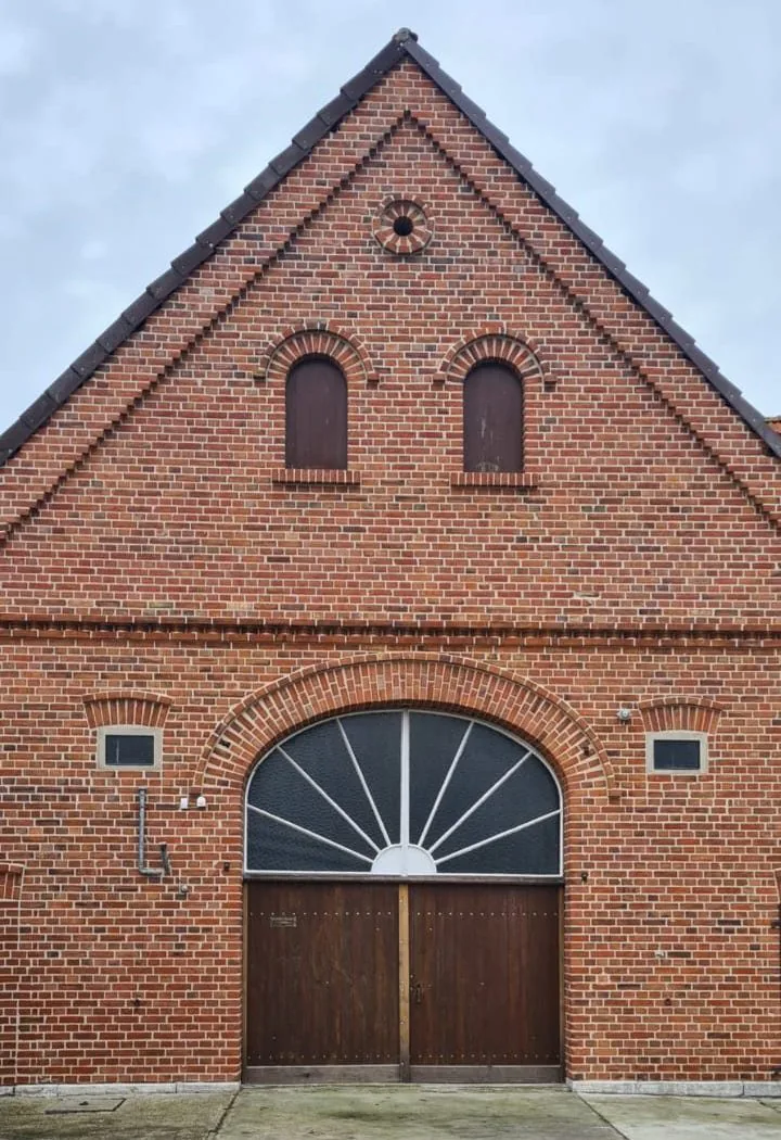 Giebel einer Klinkerscheune mit Fächerfenster und Holztor nach der Sanierung