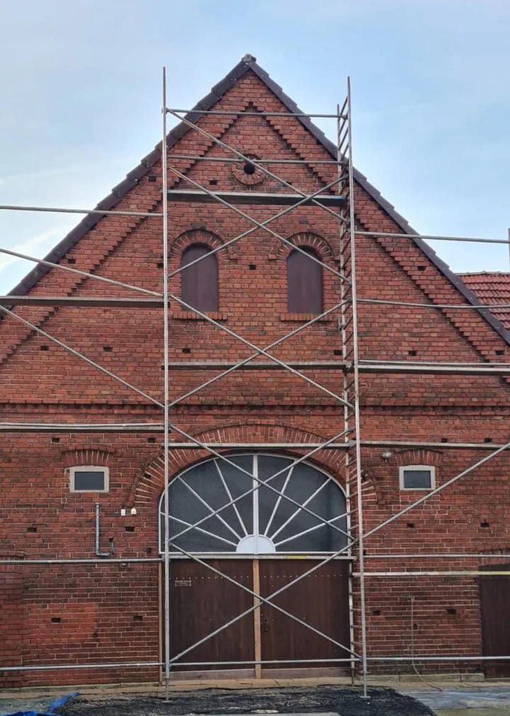 Eingerüsteter Giebel einer Klinkerscheune mit Fächerfenster und Holztor vor der Sanierung
